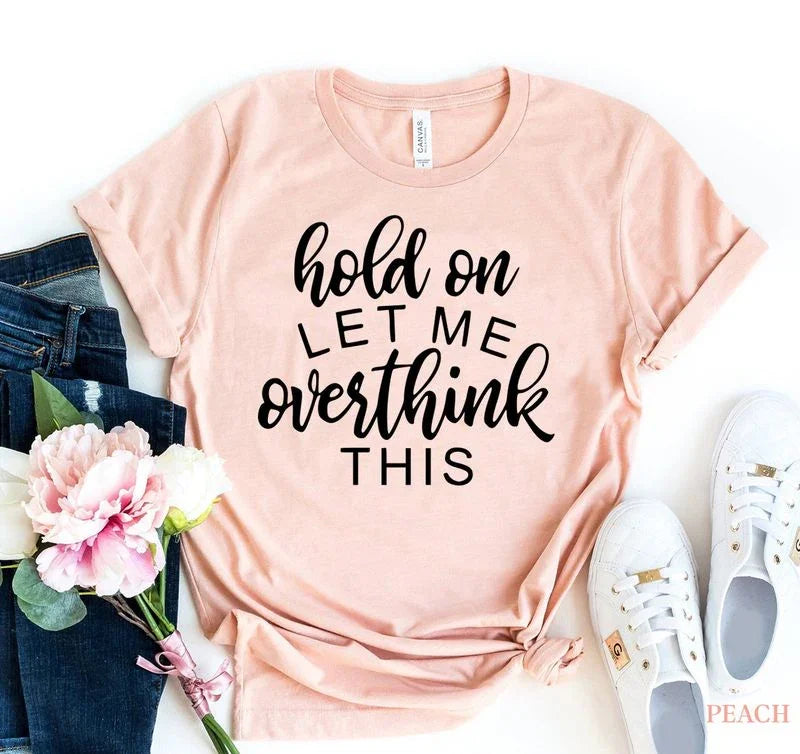 Peach graphic tee with 'hold on let me overthink this' text, styled with jeans, flowers, sneakers