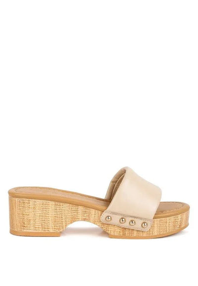 Beige platform sandal with wooden sole and gold stud accents on white background