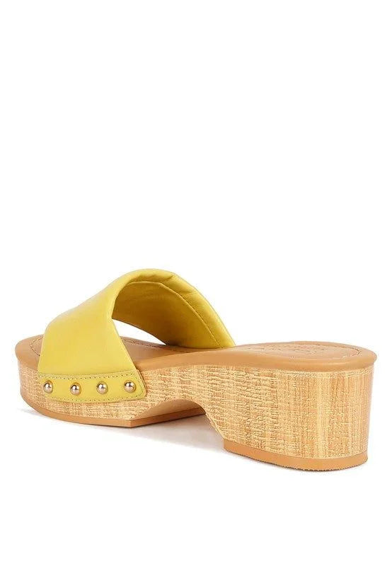 Yellow platform sandal with wooden sole, gold studs, and open back on white background