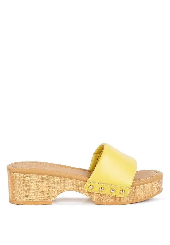 Yellow leather slide sandal with wooden block heel and gold studs on white background