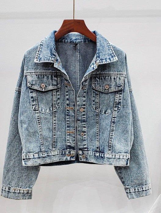 Light blue acid wash denim jacket with button front and chest pockets on hanger