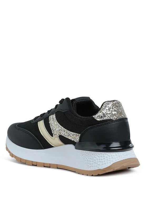Black sneaker with gold glitter accents, white sole, and gum outsole on white background.