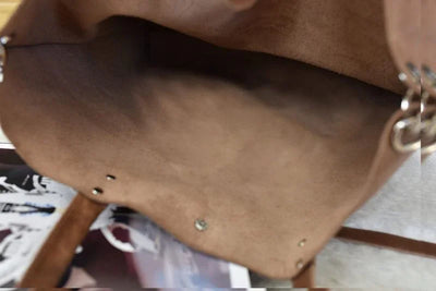 Open brown suede tote bag interior detail with metal rivets on a magazine background