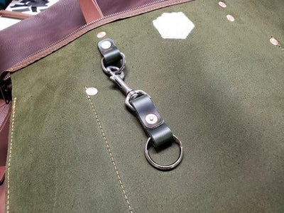 Close-up of green suede and brown leather bag with metal ring and key strap attachment