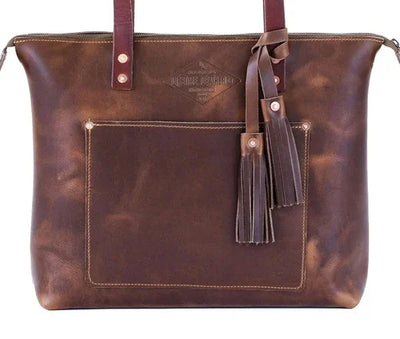 Brown leather tote bag with front pocket, tassel accents, and sturdy handles
