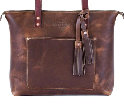 Brown full-grain leather tote bag with front pocket, tassels, and embossed logo detail