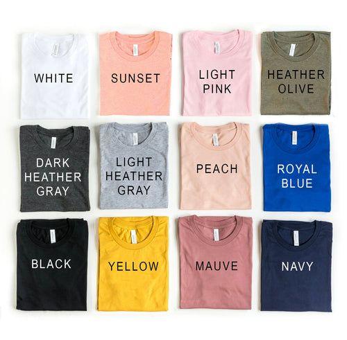 Flat lay of twelve folded t-shirts in assorted colors with color names printed on each shirt.