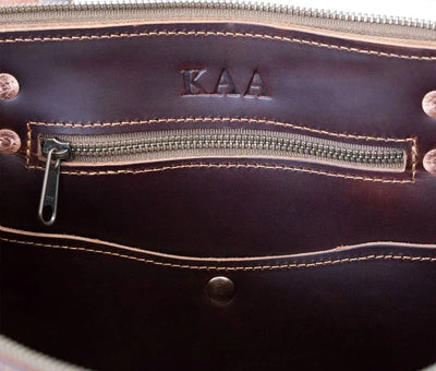 Interior of a zippered leather tote bag with KAA fire branding and stitched pocket