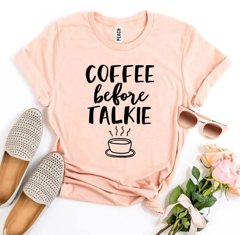 Peach t-shirt with 'Coffee Before Talkie' text, cup graphic, flat lay with shoes, sunglasses, roses