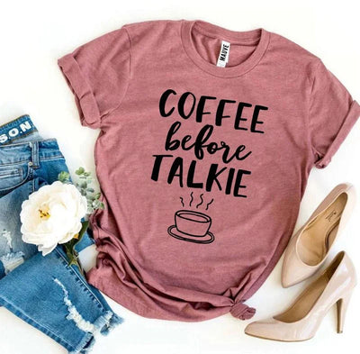 Mauve t-shirt with 'Coffee before Talkie' text, jeans, flower, and beige heels flat lay