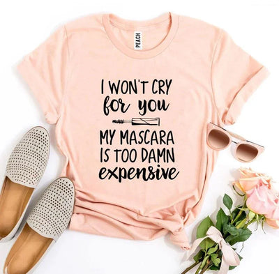 Peach t-shirt with 'I won't cry for you my mascara is too damn expensive' text, flat lay with beige loafers, sunglasses, and pink roses.