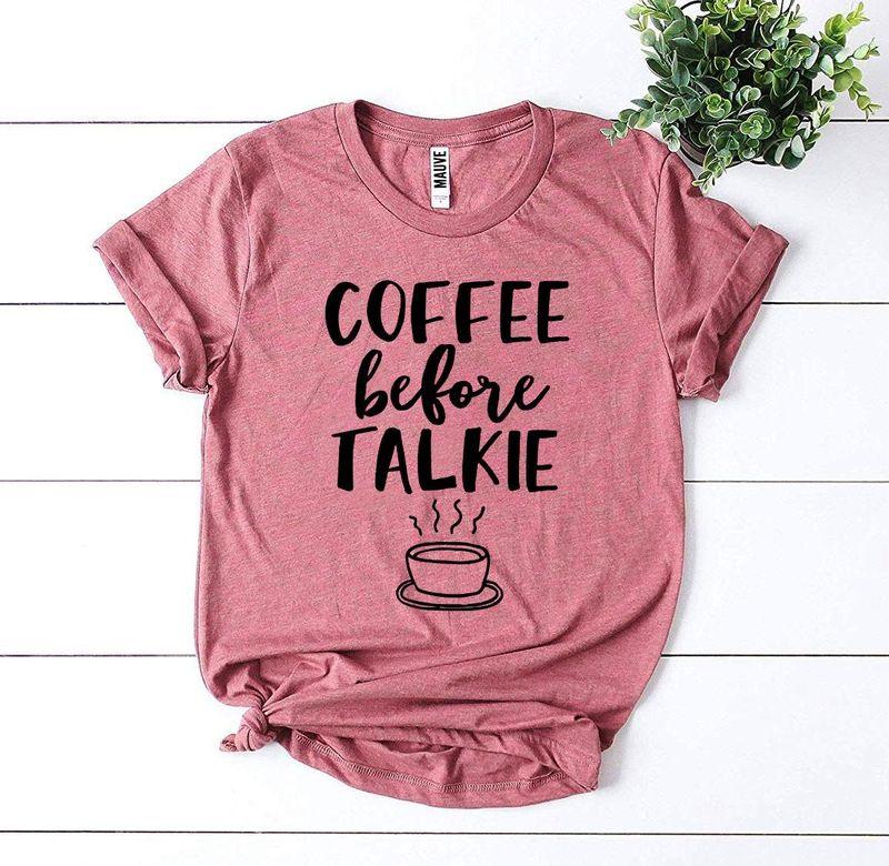 Pink graphic t-shirt with 'Coffee Before Talkie' slogan and coffee cup, flat lay with plant.