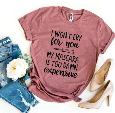 Pink graphic tee with 'I won't cry for you my mascara is too damn expensive' text, styled with ripped jeans, beige high heels, and a white flower.
