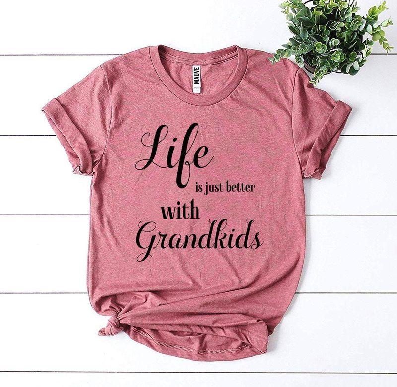 Pink t-shirt with 'Life is just better with Grandkids' text, flat lay, plant decor