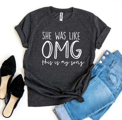 Dark gray graphic tee with 'She was like OMG this is my song' text, blue jeans, and black flats