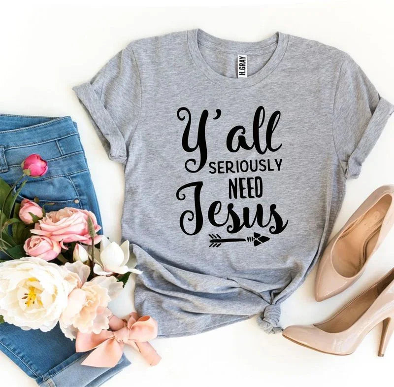 Gray t-shirt with 'Y'all seriously need Jesus' text, blue jeans, pink heels, and flowers