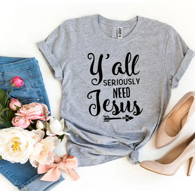Gray t-shirt with 'Y'all seriously need Jesus' text, blue jeans, pink heels, and flowers