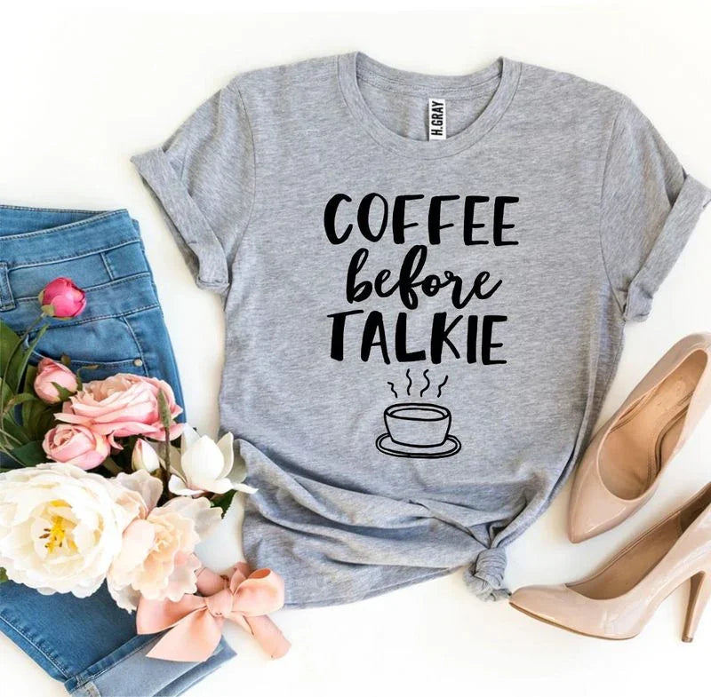 Gray t-shirt with 'Coffee before talkie' print, blue jeans, pink flowers, and beige heels.