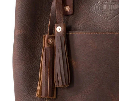 Close-up of brown leather tote bag with tassels and embossed Lifetime Leather logo